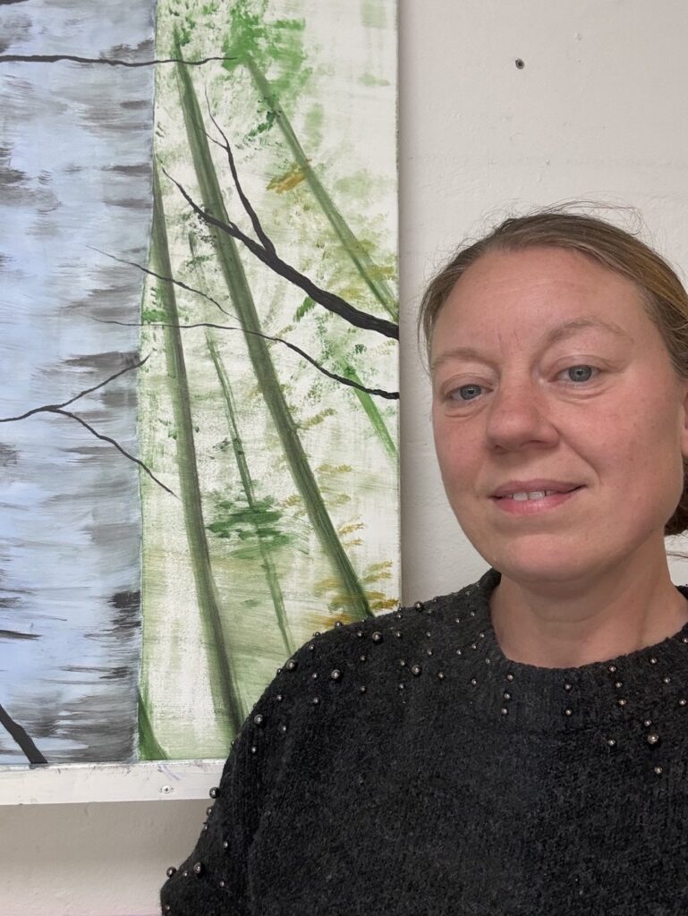 Contemporary artist Bodil Greiner stading beside one of her original nature-inspired paintings.
